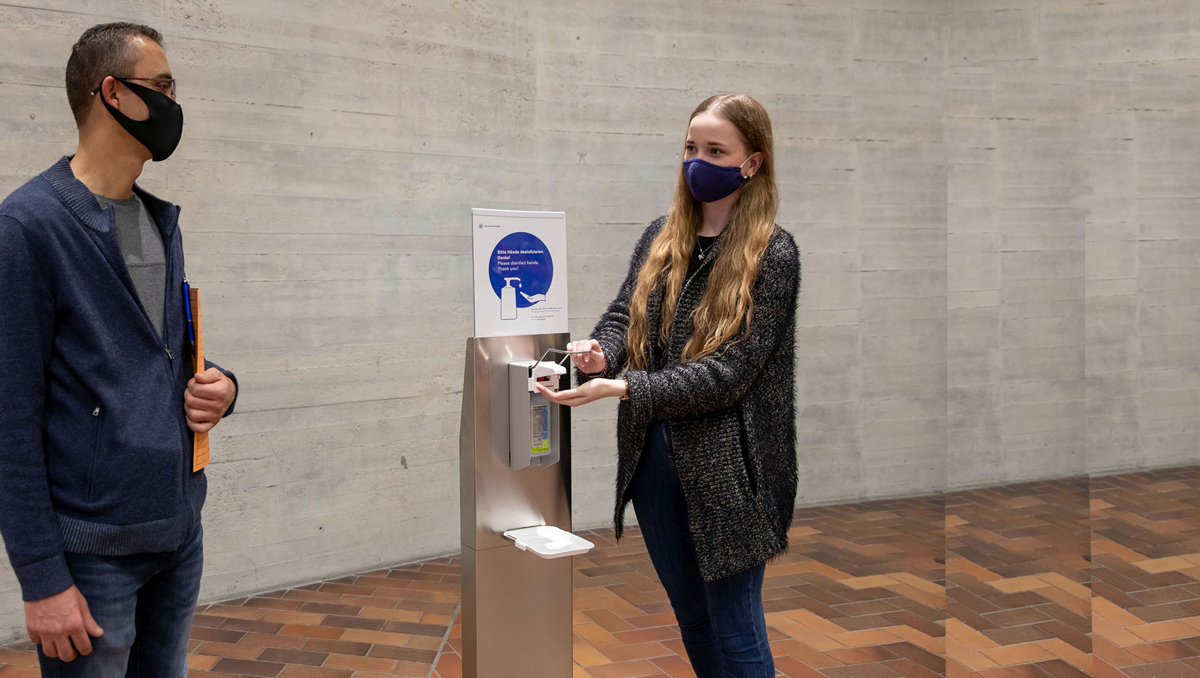 Eine Frau desinfiziert sich die Hände an einer Stelle mit Desinfektionsmitteln in einem Universitätsgebäude