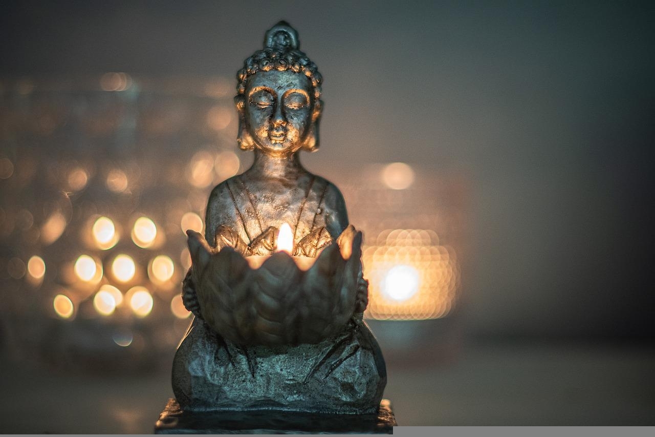 Buddhastatue mit Lotusblüte im Schoß, darin brennt eine Kerze.